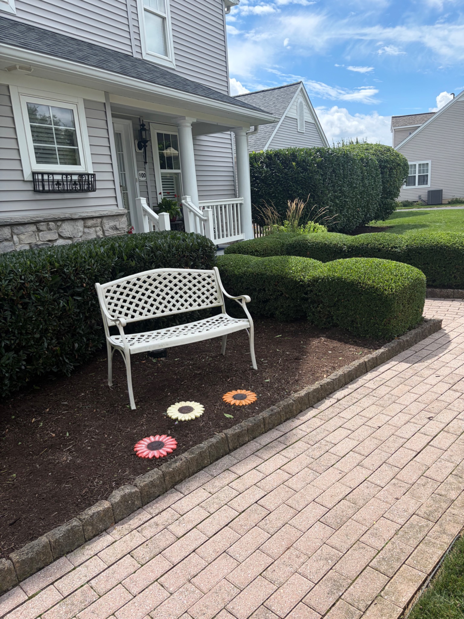 Neatly shaped shrubs beside a white garden bench and paver path